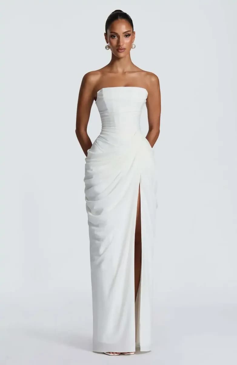 woman wearing an ivory strapless corset maxi dress with draped skirt and slit